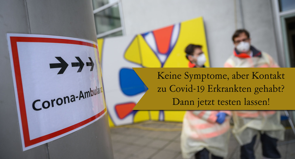 Freiwillige Mitarbeiter des Deutschen Roten Kreuzes (DRK) stehen vor der Corona-Ambulanz des Klinikums Stuttgart im Katharinenhospital, auf die ein Schild hinweist. 
