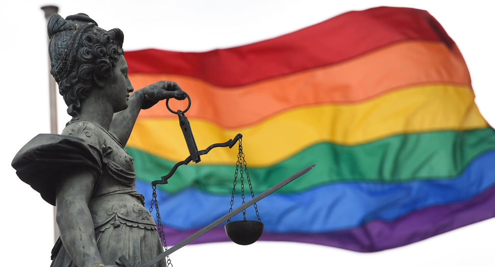 Eine Regenbogenfahne, Symbol der Lesben und Schwulen,hinter der Bronzestatue der römischen Göttin der Gerechtigkeit, Justitia (Bild: © dpa).
