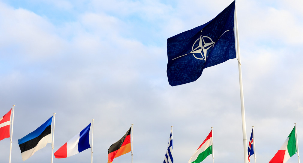 Die wehende Fahne der Nato und der Mitgliedsländer sind vor dem blauen Himmel zu sehen.