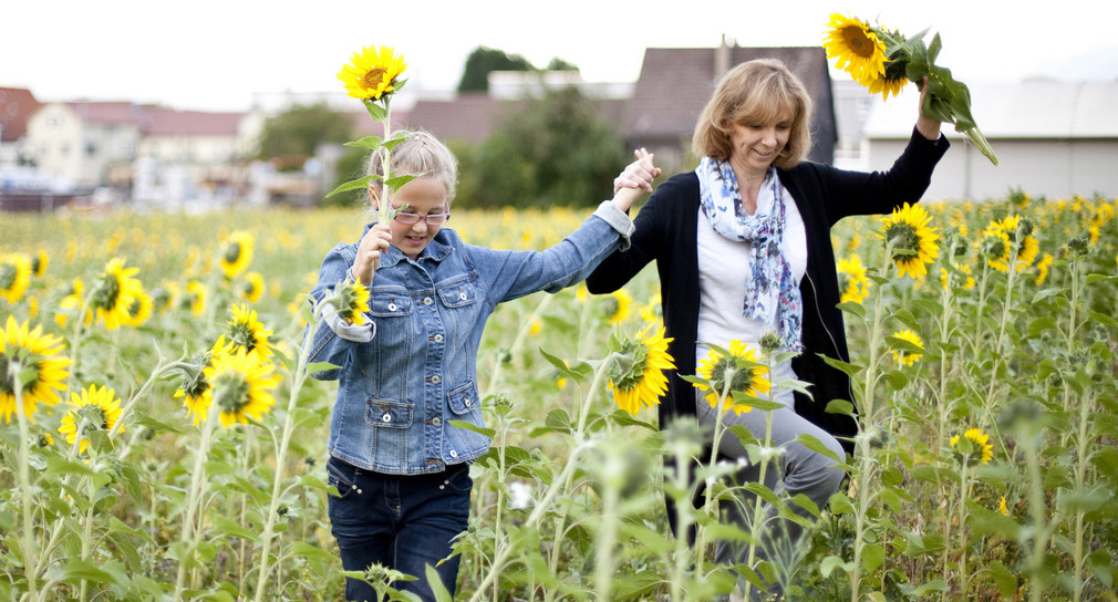 Eine Mutter die mit ihrem Kind über ein Sonnenblumenfeld läuft