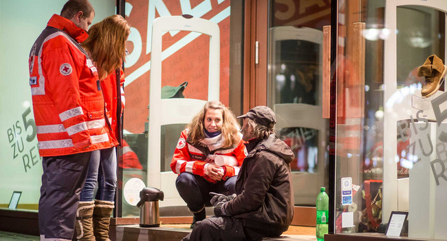 Ehrenamtliche Mitarbeiter vom Deutschen Roten Kreuz (DRK) und Teil des Teams vom Kältebus, versorgen am frühen Morgen auf der Königstrasse in Stuttgart einen Obdachlosen mit heißem Tee.']