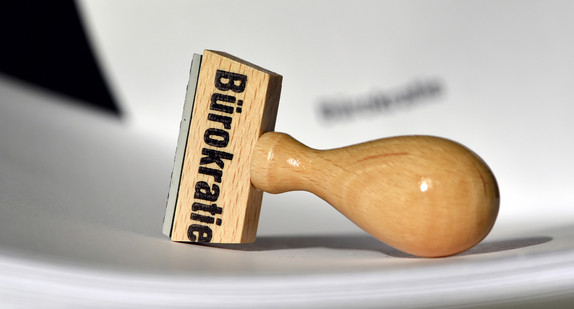 Ein Stempel mit der Aufschrift &amp;amp;quot;Bürokratie&amp;amp;quot; liegt auf Papieren.