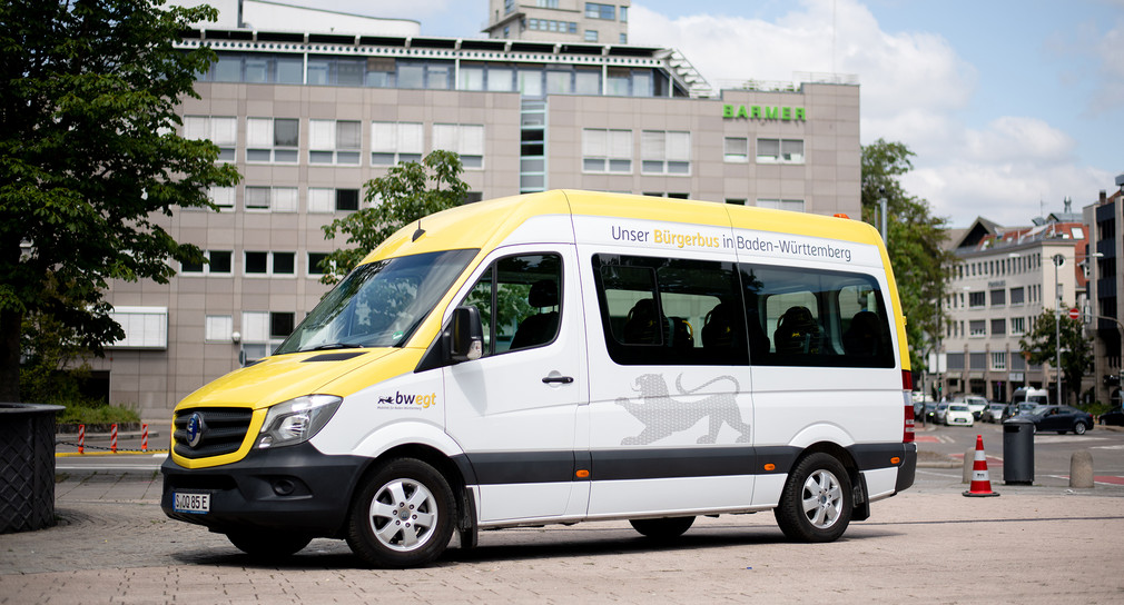 Ein kleiner weiß, gelber Transporter steht als Bürgerbus umgebaut auf einem Platz.