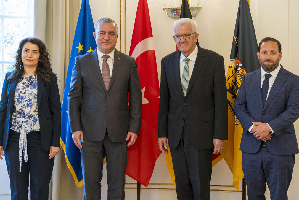 von links nach rechts: Generalkonsulin Makbule Koçak, Botschafter Ahmet Başar Şen, Ministerpräsident Winfried Kretschmann und Staatssekretär Florian Hassler stehen in der Villa Reitzenstein vor Fahnen.