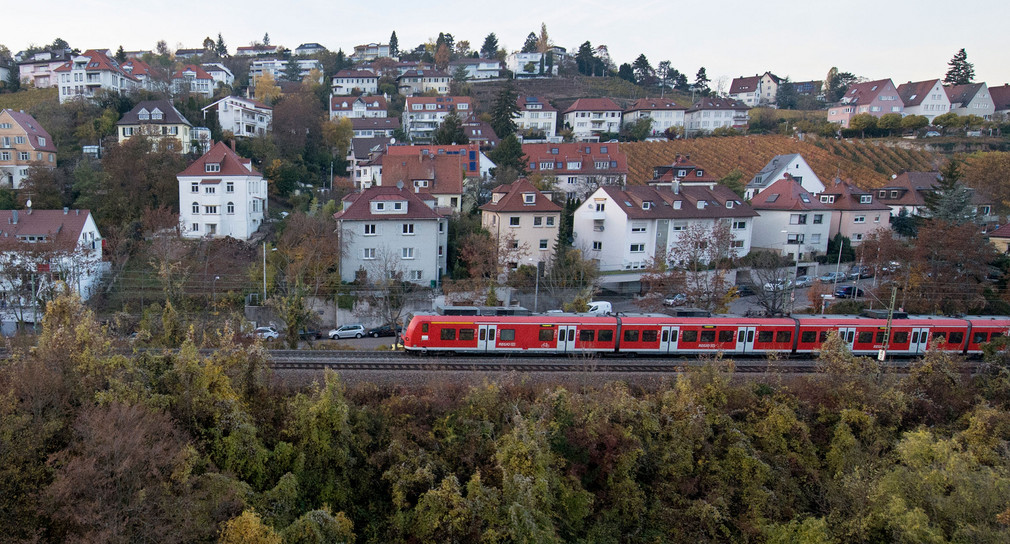 Ein Zug fährt an einem mit Häusern übersäten Hügeln durch eine grüne Landschaft.