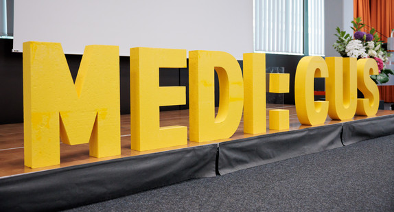 Schriftzug „MEDI:CUS“ auf einer Bühne