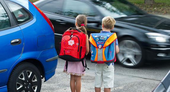 Zwei Grundschüler stehen an einer Straße vor einer Schule.