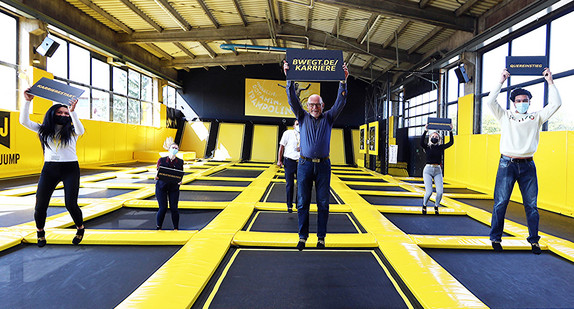 Minister Hermann springt auf einem großen Trampolin und hält ein Schild hoch.