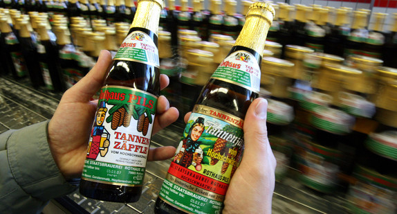 Ein Mann hält neben der Abfüllanlage zwei Flaschen Tannenzäpfle Bier der Rothaus Brauerei in der Hand (Bild: © dpa).