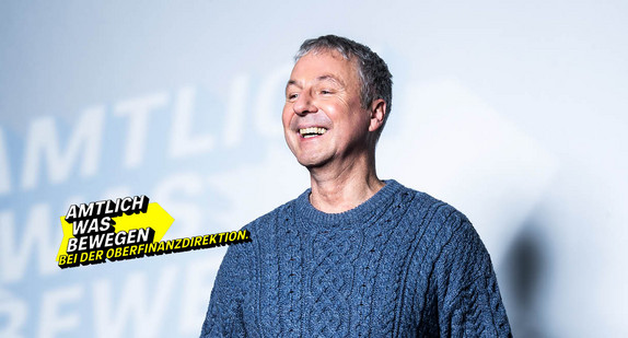 Lächelnder Mann mittleren Alters in einem Strickpullover symbolisiert die Oberfinanzdirektion.