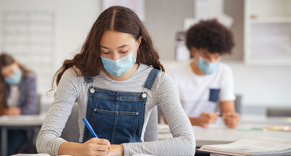 Eine Schülerin sitzt mit einer medizinischen Maske während einer Prüfung im Klassenzimmer.