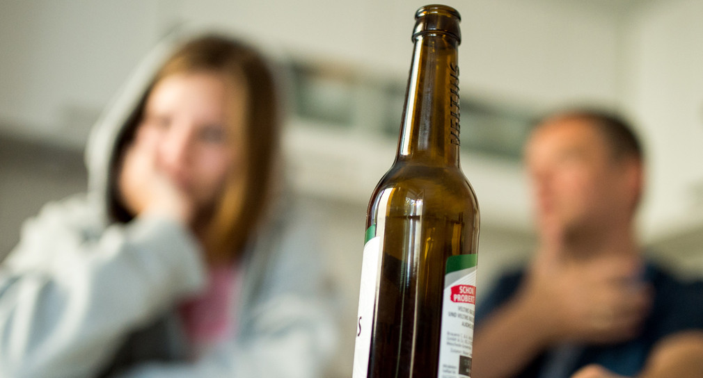 Ein Mädchen streitet mit ihrem Vater, während im Vordergrund eine Bierflasche steht. (Foto: © dpa)