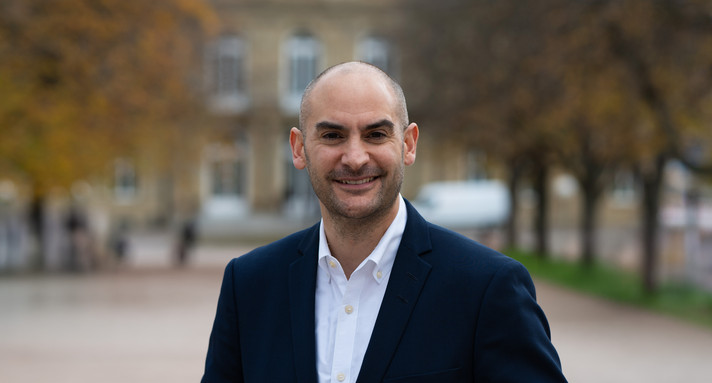Finanzminister Danyal Bayaz am Schlossplatz in Stuttgart, im Hintergrund das Neue Schloss sowie herbstliche Bäume.