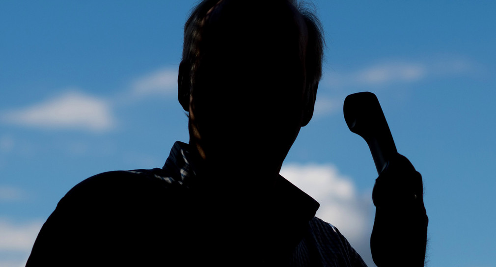 Ein von Schatten bedeckter Mann vor blauem Himmel hält ein Telefon in der Hand