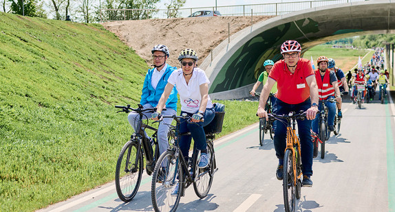 Eine große Kolonne von Fahrradfahrerinnen und -fahrern radeln auf einem neuem Radweg. Die Personen tragen alle einen Helm. 