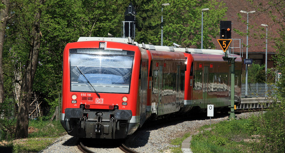 Ein roter Diesel-Personenzug fährt auf einem Gleis entgegen.