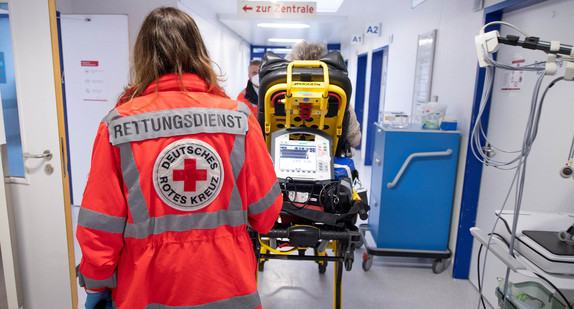 Miriam Görg, Notfallsanitäterin des Deutschen Roten Kreuzes (DRK), schiebt eine Seniorin nach einem Schlaganfall auf einer Trage in die Notaufnahme eines Krankenhauses.