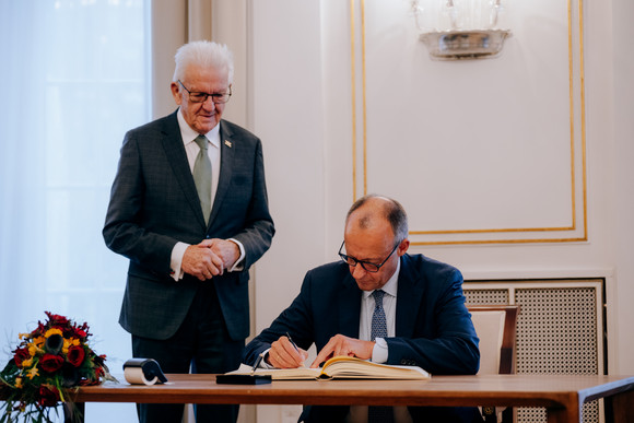 Bundeskanzler Friedrich Merz (rechts) beim Eintrag in das Gästebuch des Landes, daneben steht Ministerpräsident Winfried Kretschmann (links)