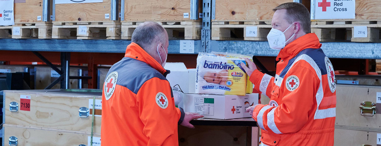 Mitarbeiter des Deutschen Roten Kreuzes (DRK) betrachten Hilfsgüter, die für einen Transport verladen werden sollen. 