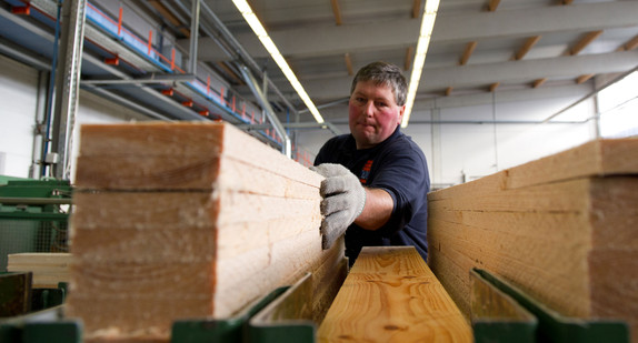 Ein Arbeiter sortiert einen Stapel Holzbretter in eine automatische Maschine in einer Holzbaufirma.