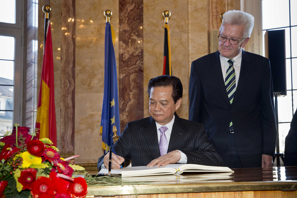 Der Premierminister von Vietnam, Nguyen Tan Dung (l.), trägt sich in das Gästebuch des Landes ein. Ministerpräsident Winfried Kretschmann (r.) steht daneben.