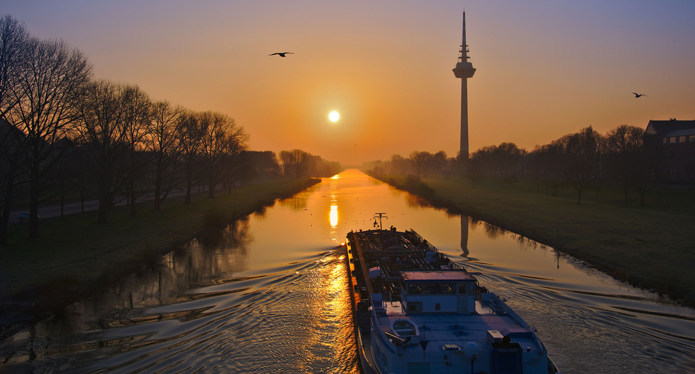 Ein Frachtschiff fährt bei Sonnenaufgang auf dem Neckar bei Mannheim in Richtung des Fernsehturms.