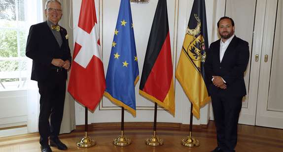 Staatssekretär Florian Hassler (r.) und der Schweizer Botschafter Dr. Paul Seger (l.) stehen neben Fahnen.