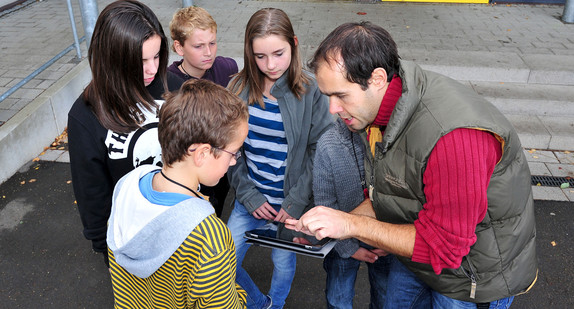 Ein Schulsozialarbeiter erklärt Kindern die Regeln für Geocaching. (Foto: dpa)