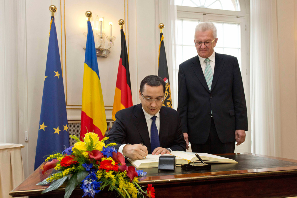 Der Premierminister von Rumänien, Victor-Viorel Ponta (l.), trägt sich in das Gästebuch des Landes ein. Daneben steht Ministerpräsident Winfried Kretschmann (r.).