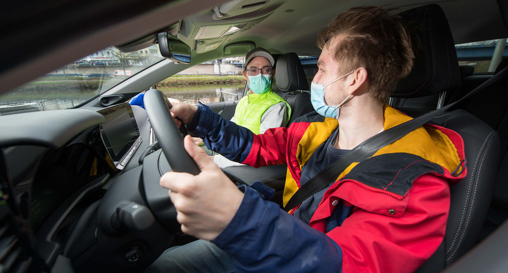 Ein Fahrschüler und ein Fahrlehrer sitzen mit Mund-Nasen-Schutz in einem Auto.
