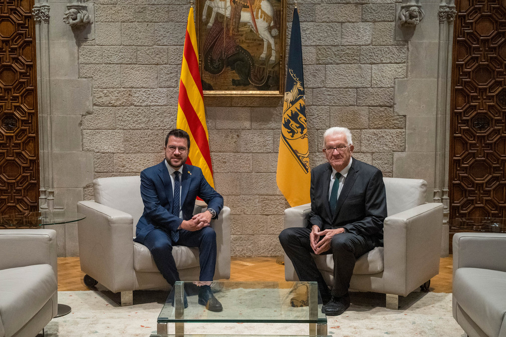 Ministerpräsident Winfried Kretschmann (rechts) und Regionalpräsident Pere Aragonès (links) sitzen vor einer baden-württembergischen und einer katalonischen Fahne. 