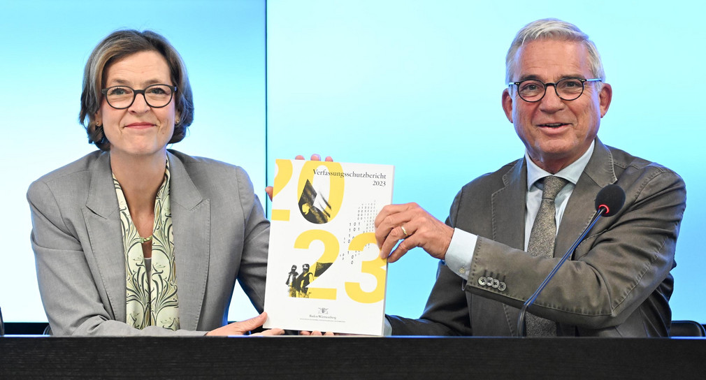 Innenminister Thomas Strobl (rechts) und Beate Bube (links), Präsidentin des Landesamtes für Verfassungsschutz Baden-Württemberg, halten im Landtag bei der Vorstellung des Verfassungsschutzberichts 2023 den gedruckten Bericht in ihren Händen.