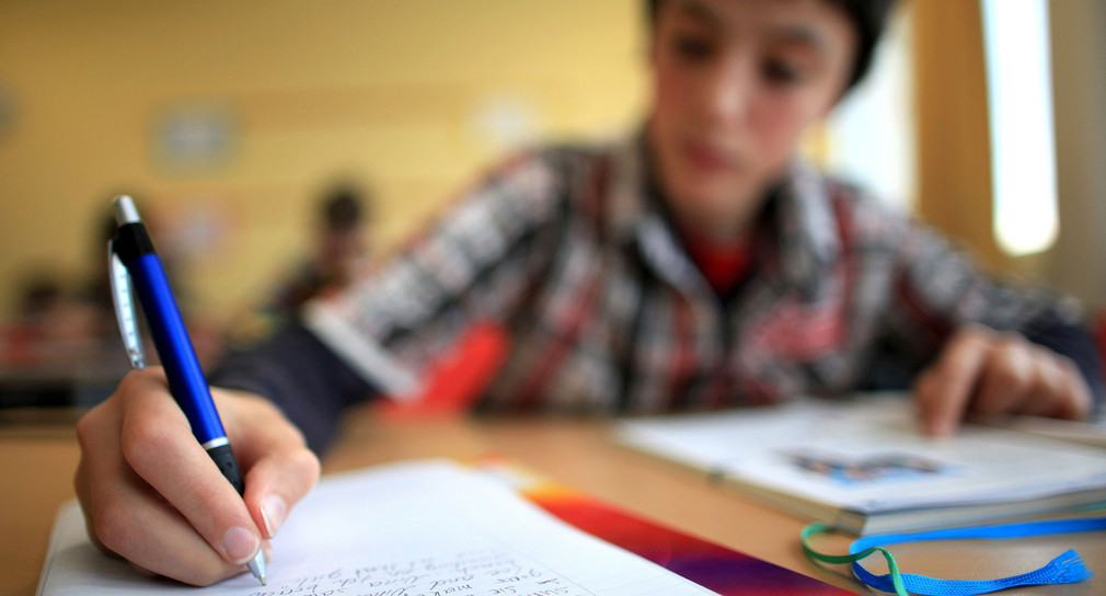 Ein Schüler schreibt im Unterricht einen Text in sein Heft (Bild: © dpa).