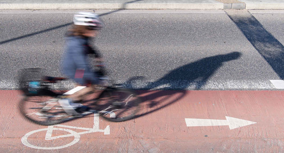 Ein Fahrradfahrer fährt auf einem Radweg, der an einer Straße entlang läuft.