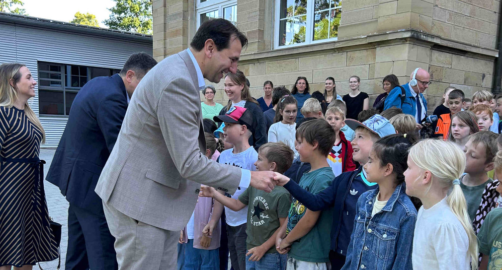 Kultusminister Jung (Mitte) mit Grundschulkindern. Der Minister schüttelt einem Jungen die Hand.