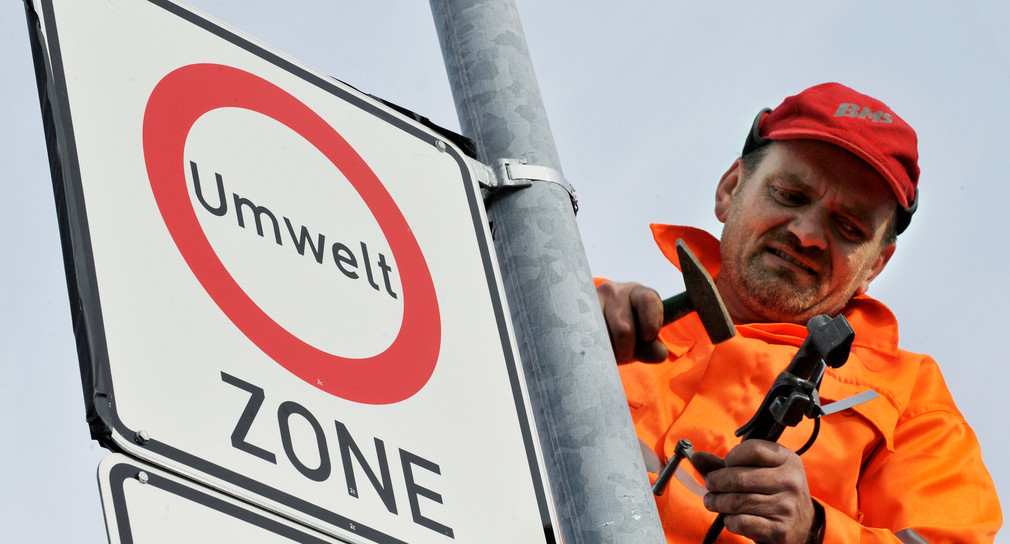 Ein Mitarbeiter einer Straßenschilderfirma befestigt in Freiburg ein Verkehrsschild, das auf eine Umweltzone in der Innenstadt hinweist (Bild: dpa).