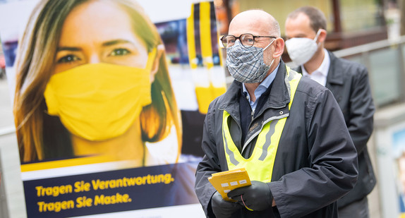 Verkehrsminister Winfried Hermann steht neben einem Schild mit der Aufschrift "Tragen Sie Verantwortung. Tragen Sie Maske". (Bild: © picture alliance/Sebastian Gollnow/dpa)