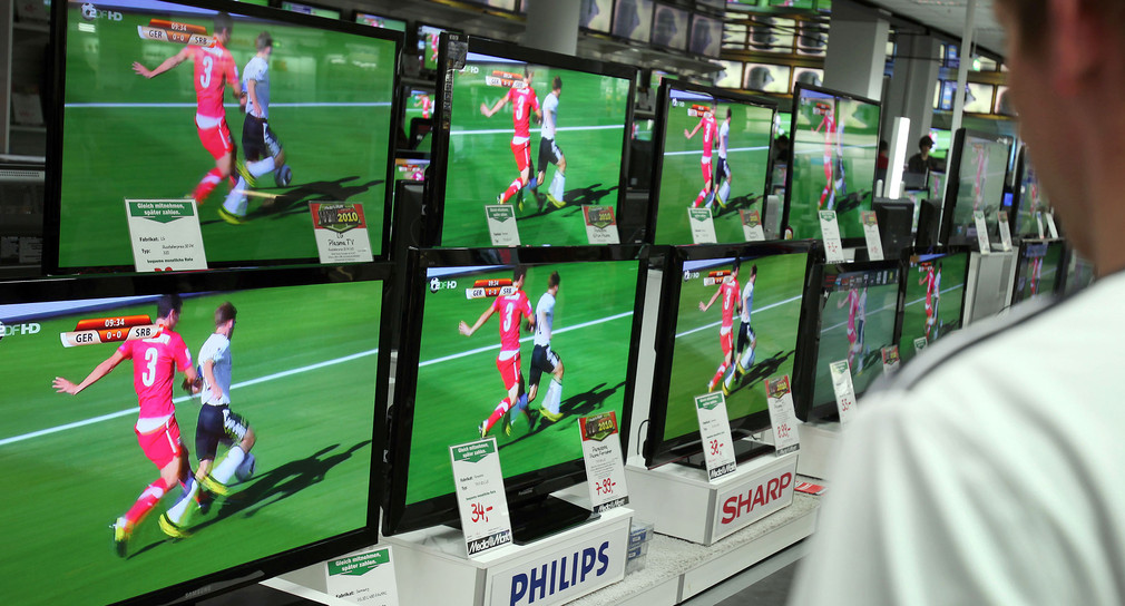 Ein Mensch steht in einem Elektronikfachmarkt vor einer Auswahl an Fernsehgeräten.