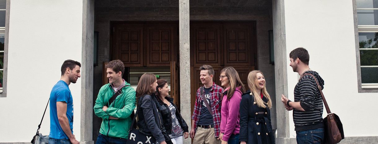 Studierende stehen vor einem Gebäude an der Universität Heidelberg (Bild: © Shooresh Fezoni).