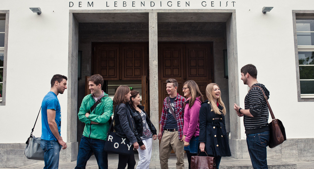 Studierende stehen vor einem Gebäude an der Universität Heidelberg (Bild: © Shooresh Fezoni).