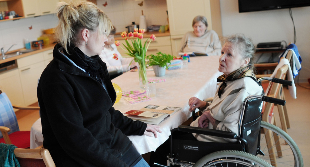 Eine Altenpflegerin spricht mit Senioren in einer Pflege-Wohngemeinschaft für Demenzkranke.