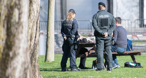 Polizeibeamte sprechen im Schlossgarten mit einer Gruppe von vier Leuten, die an einem Tisch sitzt (Bild: © picture alliance/Sebastian Gollnow/dpa)