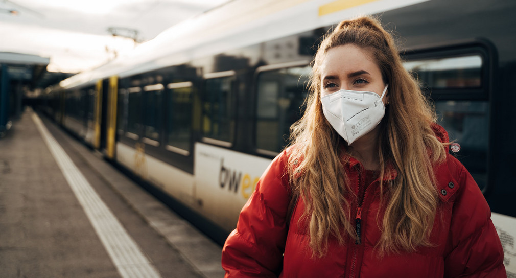 Frau steht auf einem Bahnsteig und trägt eine FFP2 Maske