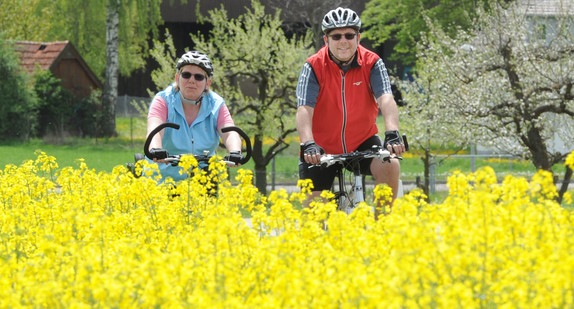 Ein Mann und eine Frau fahren mit dem Fahrrad bei Nufringen im Landkreis Böblingen an einem blühenden Rapsfeld vorbei (Bild: © dpa).