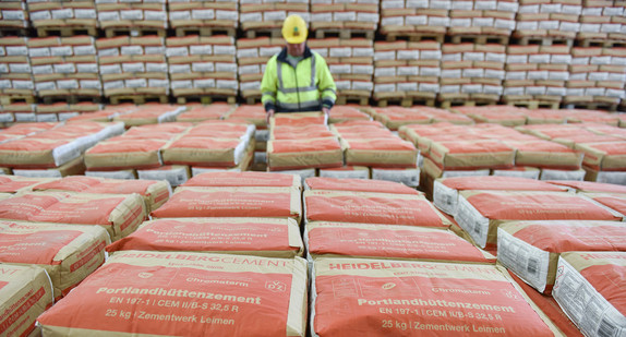 Ein Mitarbeiter steht in einem Zementwerk zwischen Paletten mit Zementsäcken.