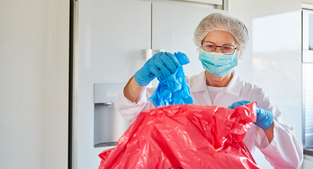 Reinigungskraft in Schutzkleidung entsorgt Einweghandschuhe in Klinik