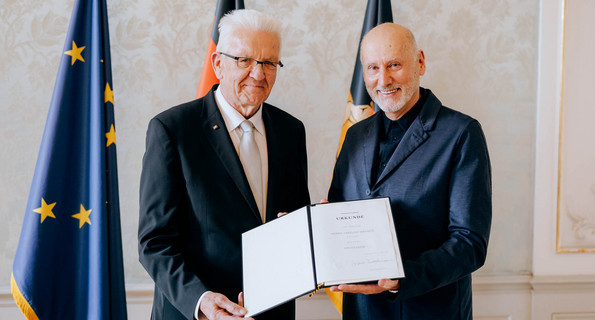 Ministerpräsident Winfried Kretschmann (links) und Tadeusz Matacz (rechts) stehen vor Fahnen und präsentieren die Verleihungsurkunde.