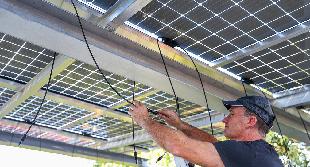 Ein Mann installiert Solarzellen auf dem Dach eines Carports.