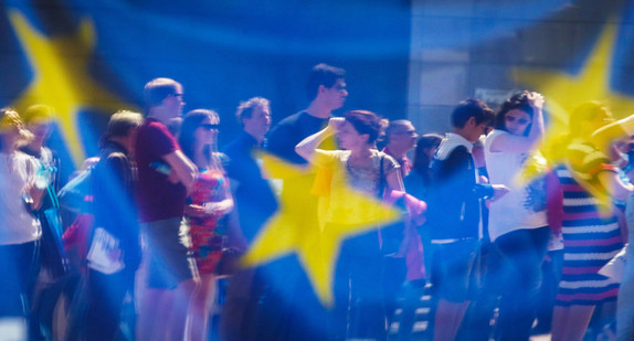 Menschen spiegeln sich in einem Fenster mit einer europäischen Flagge im Europäischen Parlament (Bild: picture alliance/Olivier Hoslet/EPA/dpa)