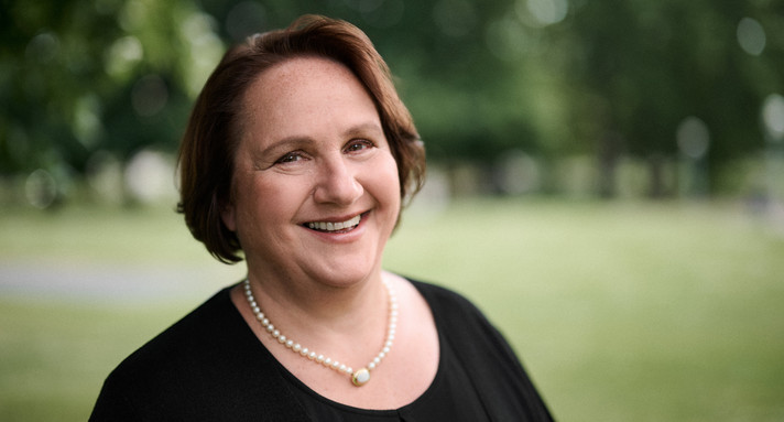 Portraitaufnahme von Ministerin Schopper. Im Hintergrund ist verschwommen der Schlossgarten zu sehen